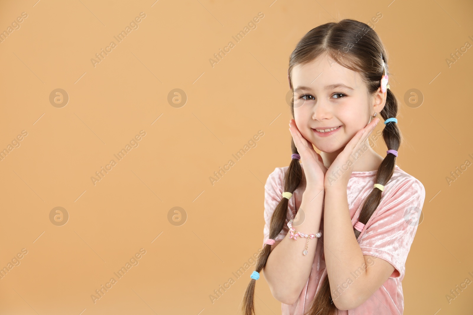 Photo of Little girl wearing beautiful hair accessories on beige background, space for text