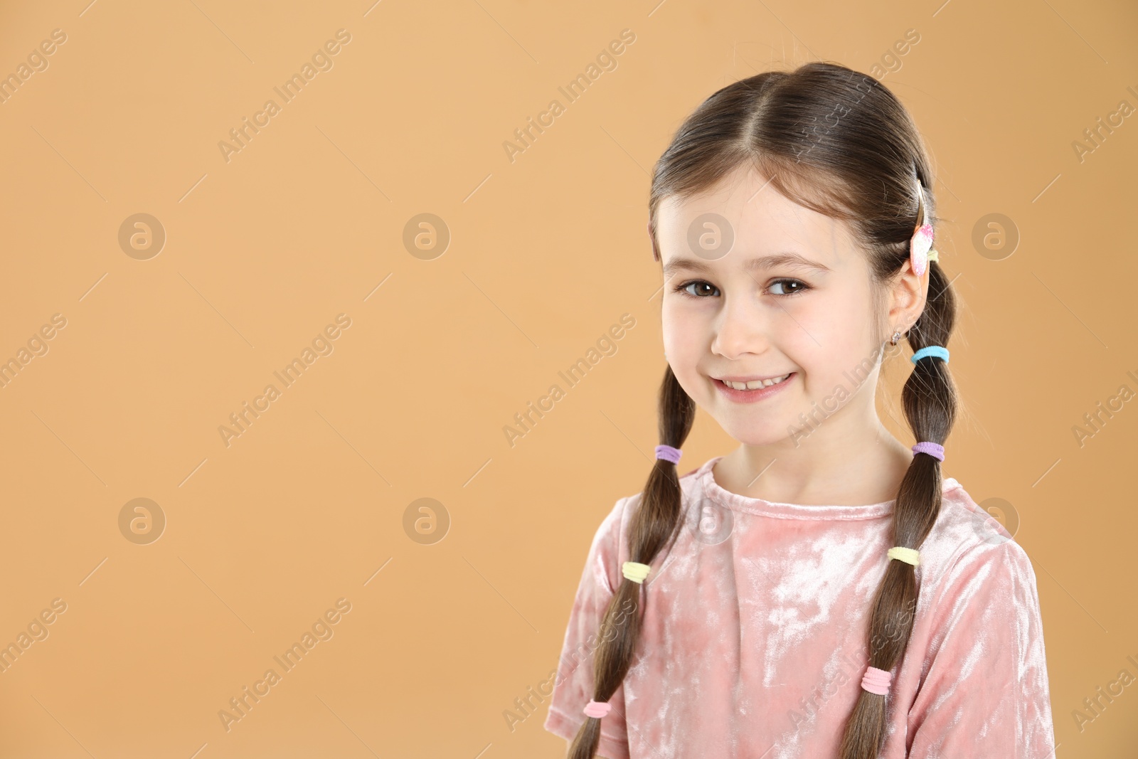 Photo of Little girl wearing beautiful hair accessories on beige background, space for text