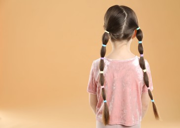 Photo of Little girl wearing beautiful hair accessories on beige background, back view. Space for text