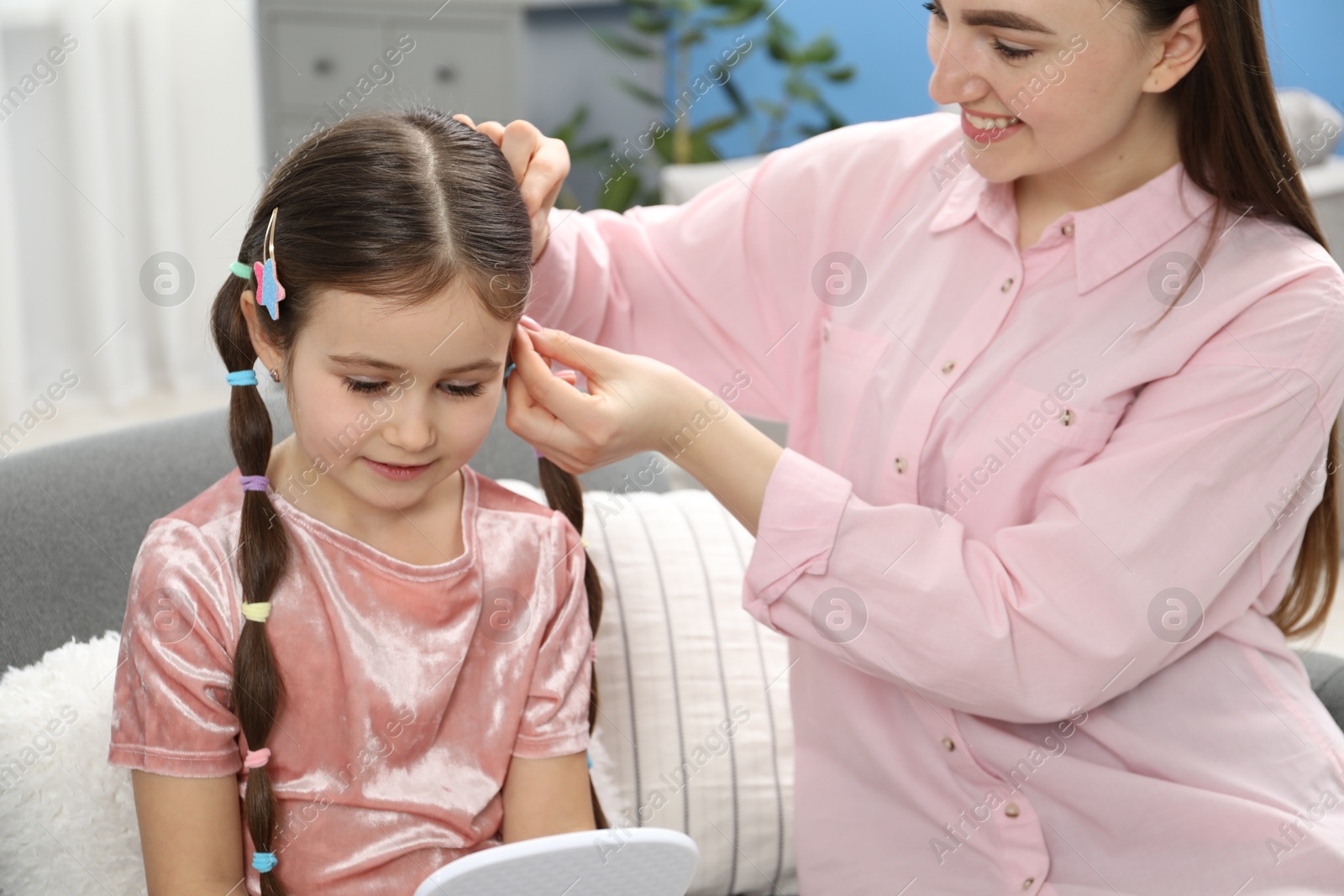 Photo of Mom putting cute accessories onto her daughter's hair at home, closeup