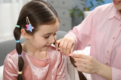 Photo of Mom putting cute accessories onto her daughter's hair at home, closeup