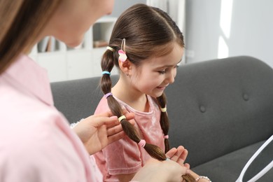 Photo of Mom putting cute accessories onto her daughter's hair at home, closeup