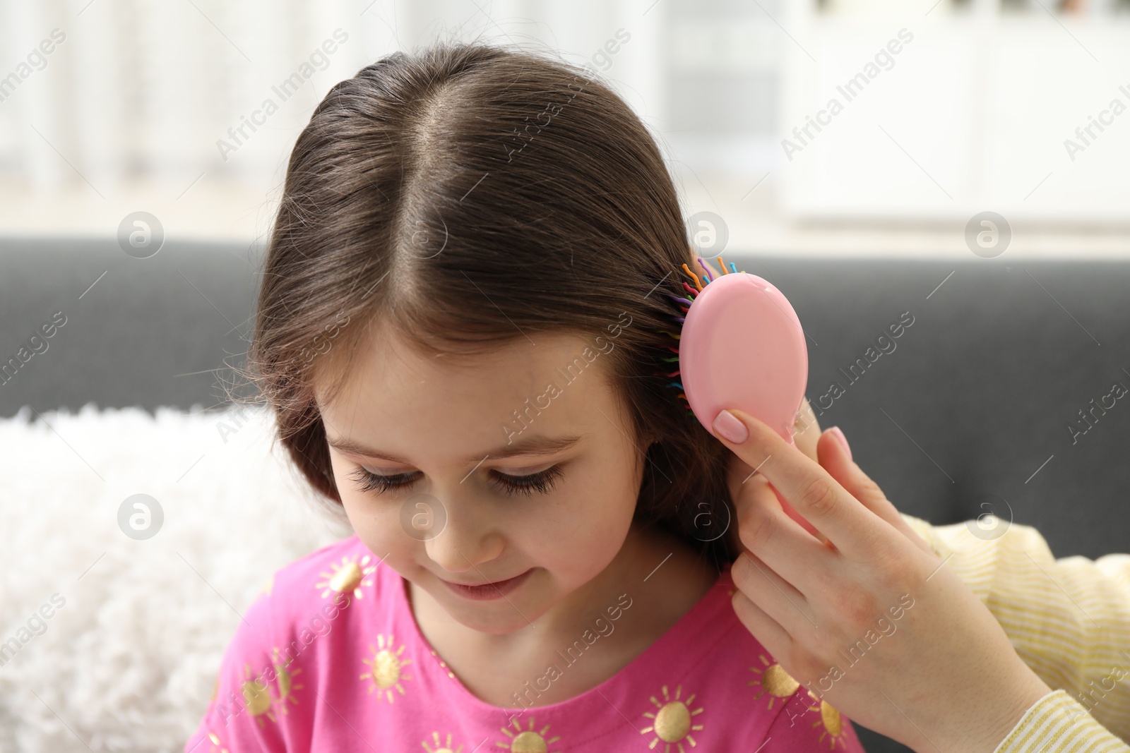 Photo of Mother brushing her little daughter's hair at home, closeup