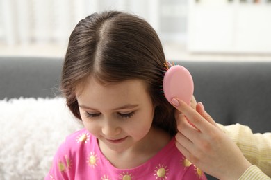 Photo of Mother brushing her little daughter's hair at home, closeup