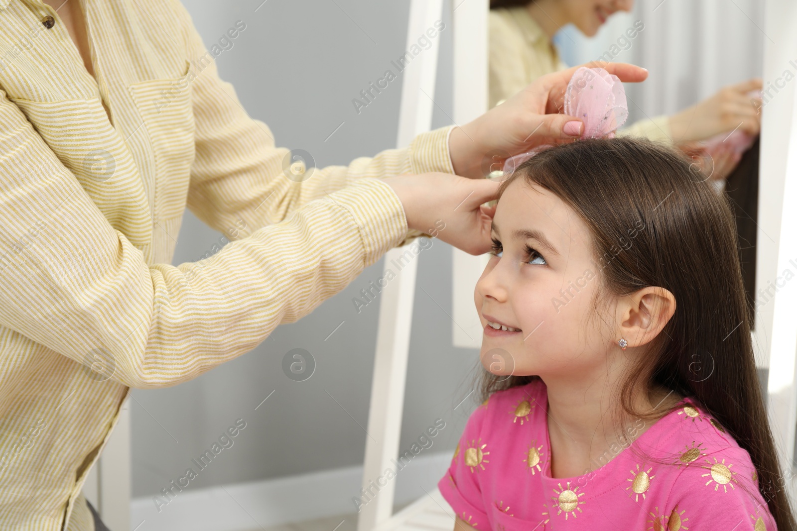 Photo of Mom putting cute accessories onto her daughter's hair at home, closeup