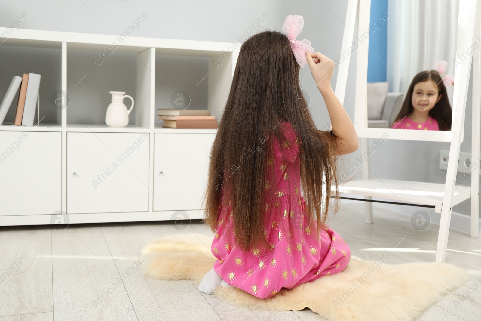 Photo of Little girl wearing beautiful hair clip near mirror at home, selective focus