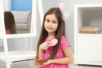 Photo of Little girl brushing her hair at home