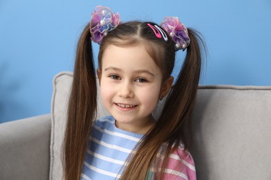 Photo of Happy little girl wearing beautiful hair accessories in armchair at home