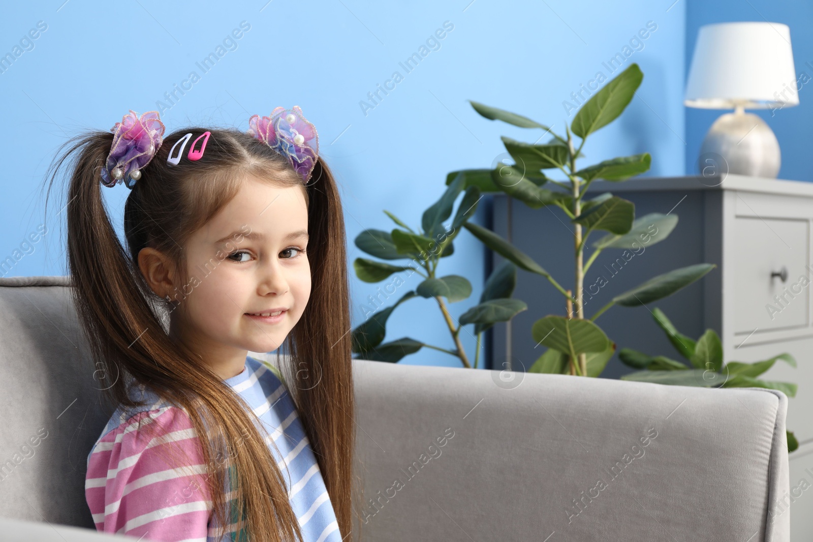 Photo of Happy little girl wearing beautiful hair accessories in armchair at home