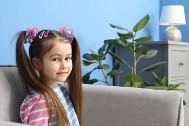 Photo of Happy little girl wearing beautiful hair accessories in armchair at home