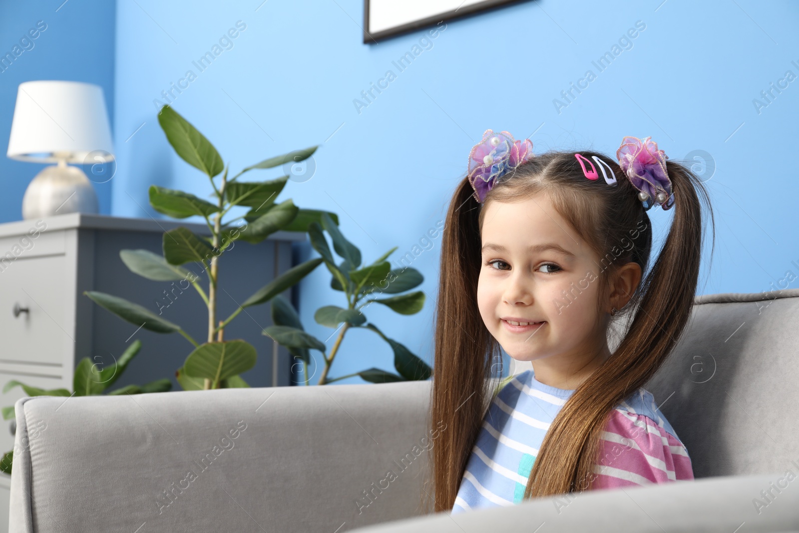 Photo of Happy little girl wearing beautiful hair accessories in armchair at home