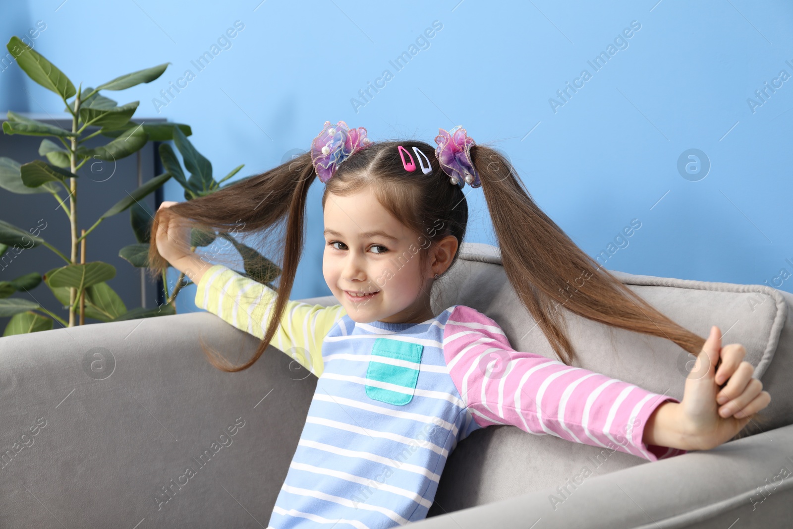 Photo of Happy little girl wearing beautiful hair accessories in armchair at home