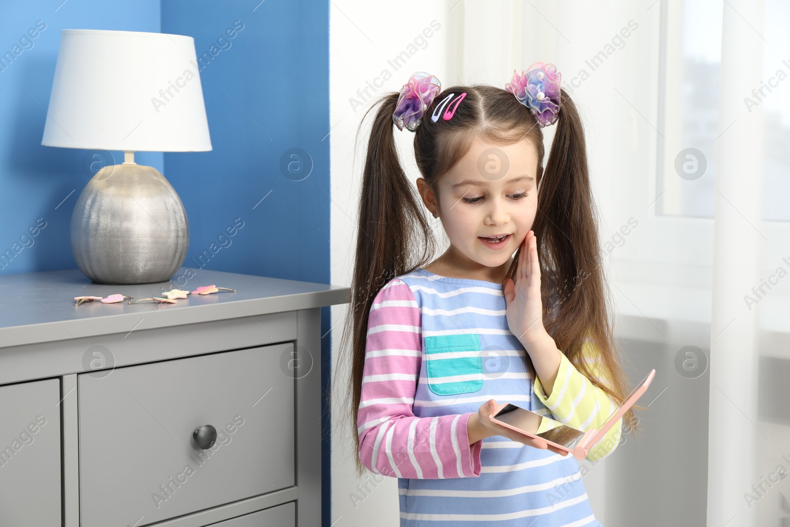 Photo of Little girl with beautiful hair accessories and pocket mirror at home