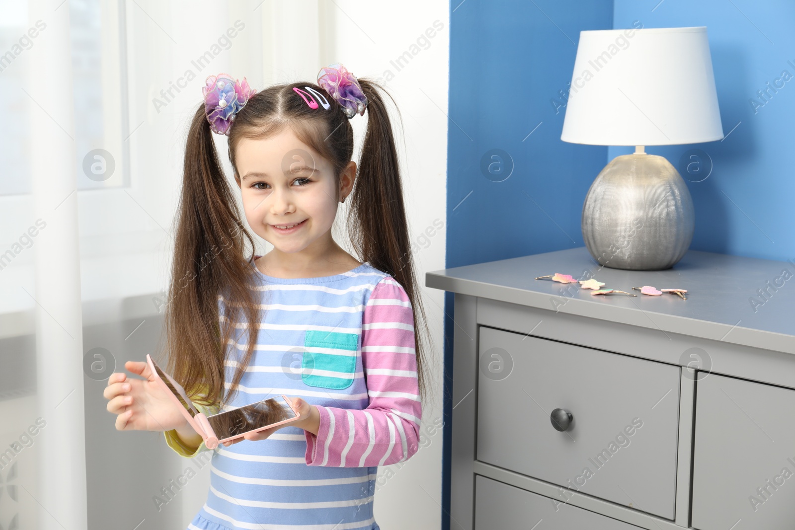 Photo of Little girl with beautiful hair accessories and pocket mirror at home