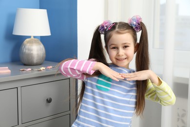 Photo of Happy little girl wearing beautiful hair accessories at home