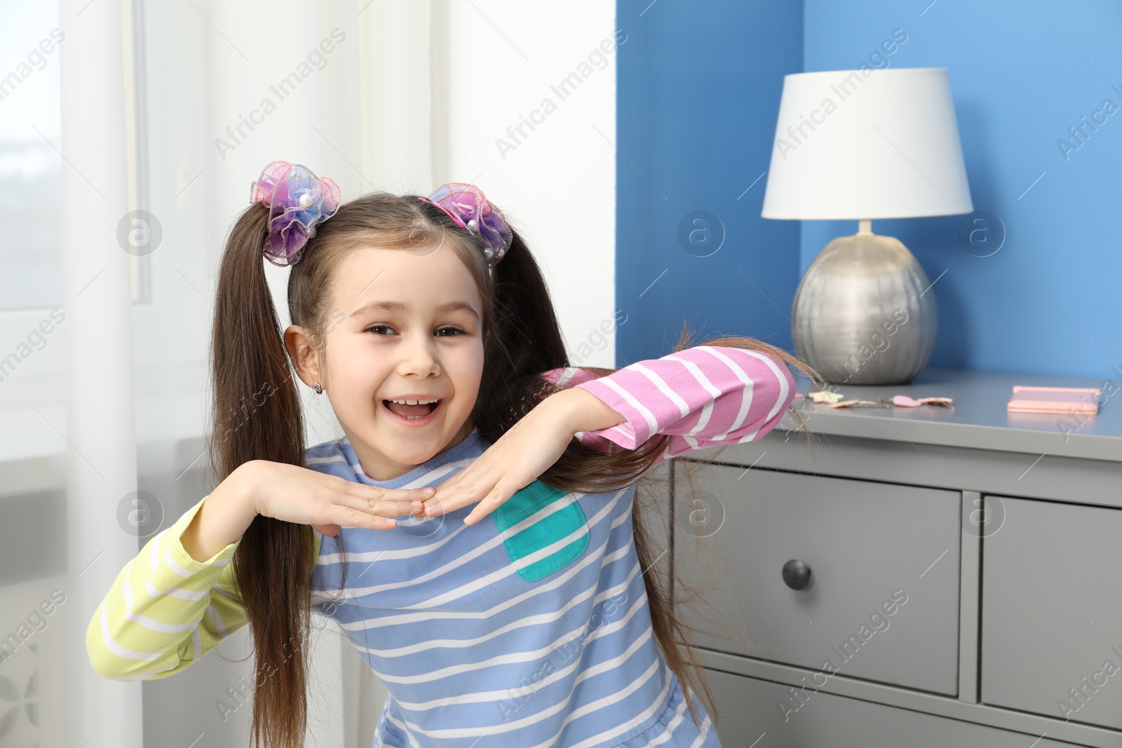 Photo of Happy little girl wearing beautiful hair accessories at home