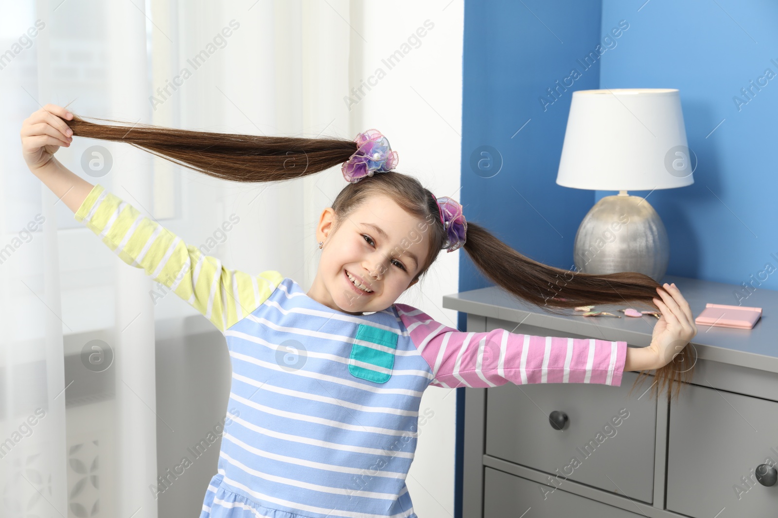 Photo of Happy little girl wearing beautiful hair accessories at home