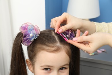 Photo of Mom putting cute accessories onto her daughter's hair at home, closeup