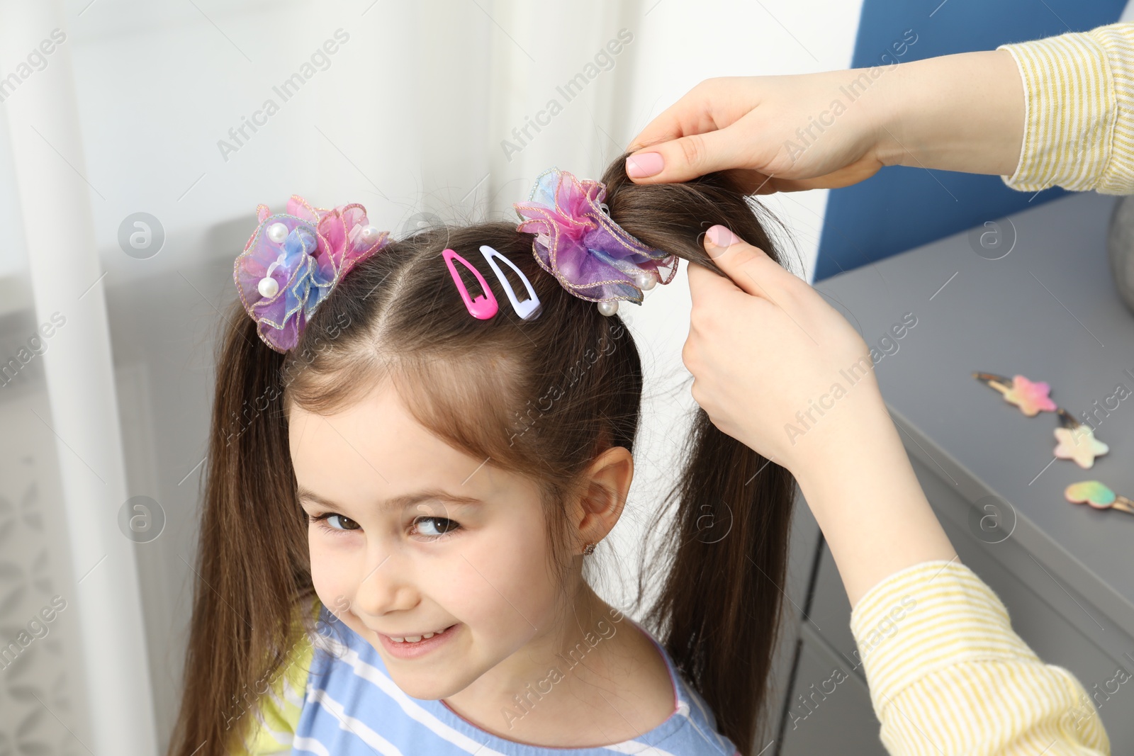 Photo of Mom putting cute accessories onto her daughter's hair at home, closeup