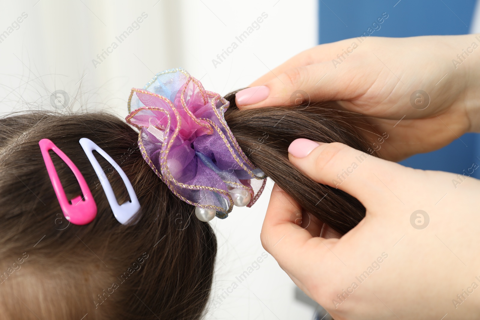 Photo of Mom putting cute accessories onto her daughter's hair at home, closeup