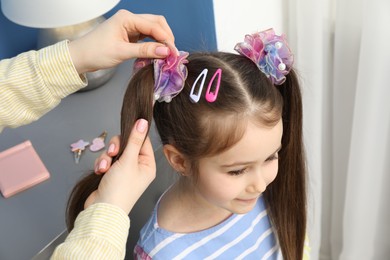 Photo of Mom putting cute accessories onto her daughter's hair at home, closeup