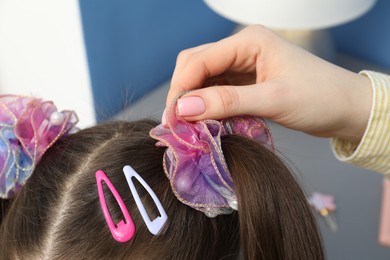 Photo of Mom putting cute accessories onto her daughter's hair at home, closeup