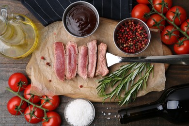 Photo of Delicious sliced beef tenderloin with different degrees of doneness, wine, tomatoes and other products on wooden table, flat lay