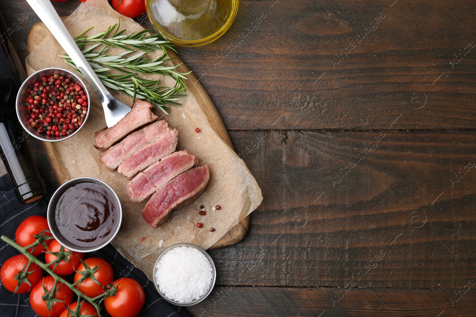 Photo of Delicious sliced beef tenderloin with different degrees of doneness, sauce, tomatoes and spices on wooden table, flat lay. Space for text