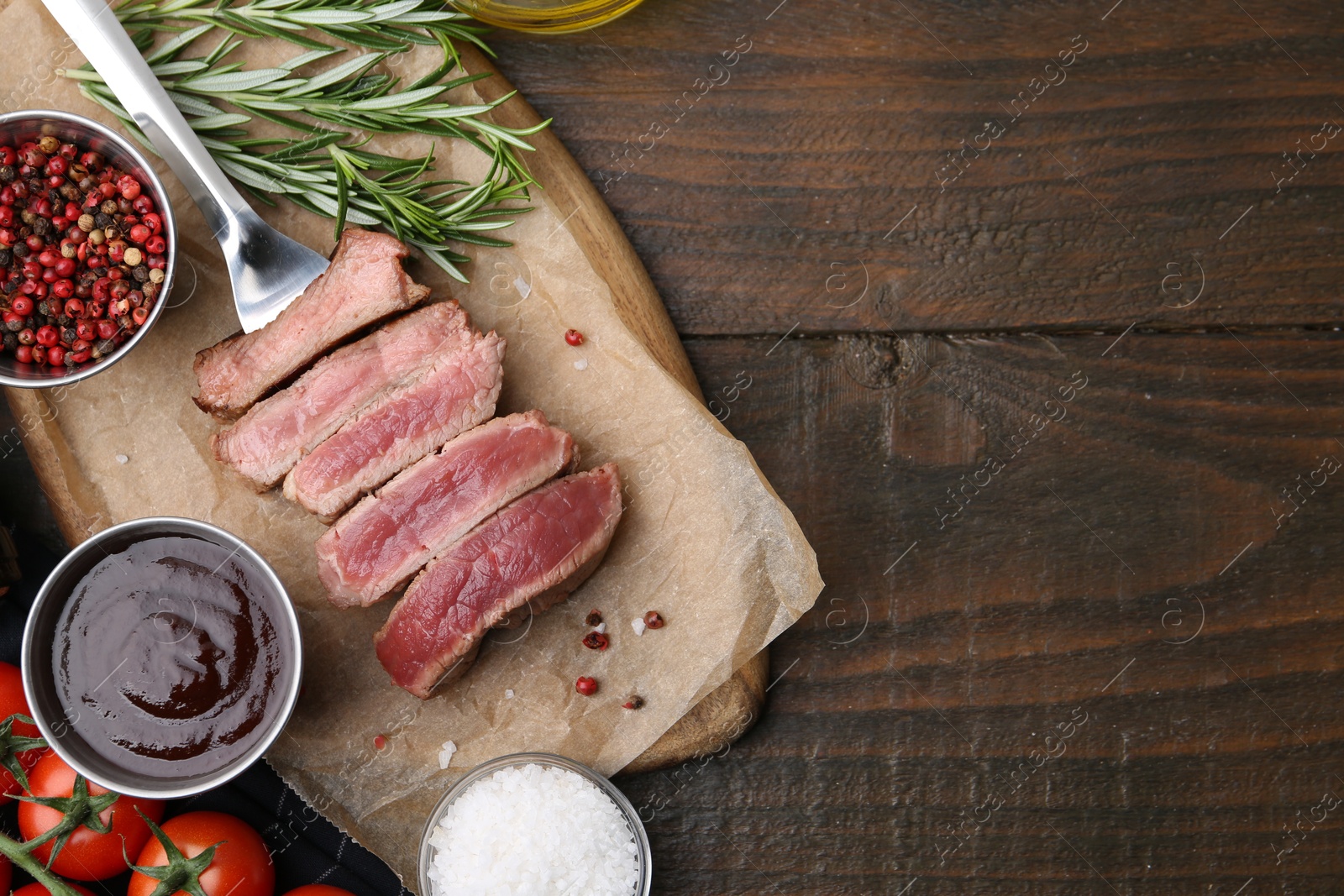 Photo of Delicious sliced beef tenderloin with different degrees of doneness, sauce, tomatoes and spices on wooden table, flat lay. Space for text