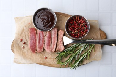 Photo of Delicious sliced beef tenderloin with different degrees of doneness, sauce and spices on light tiled table, top view