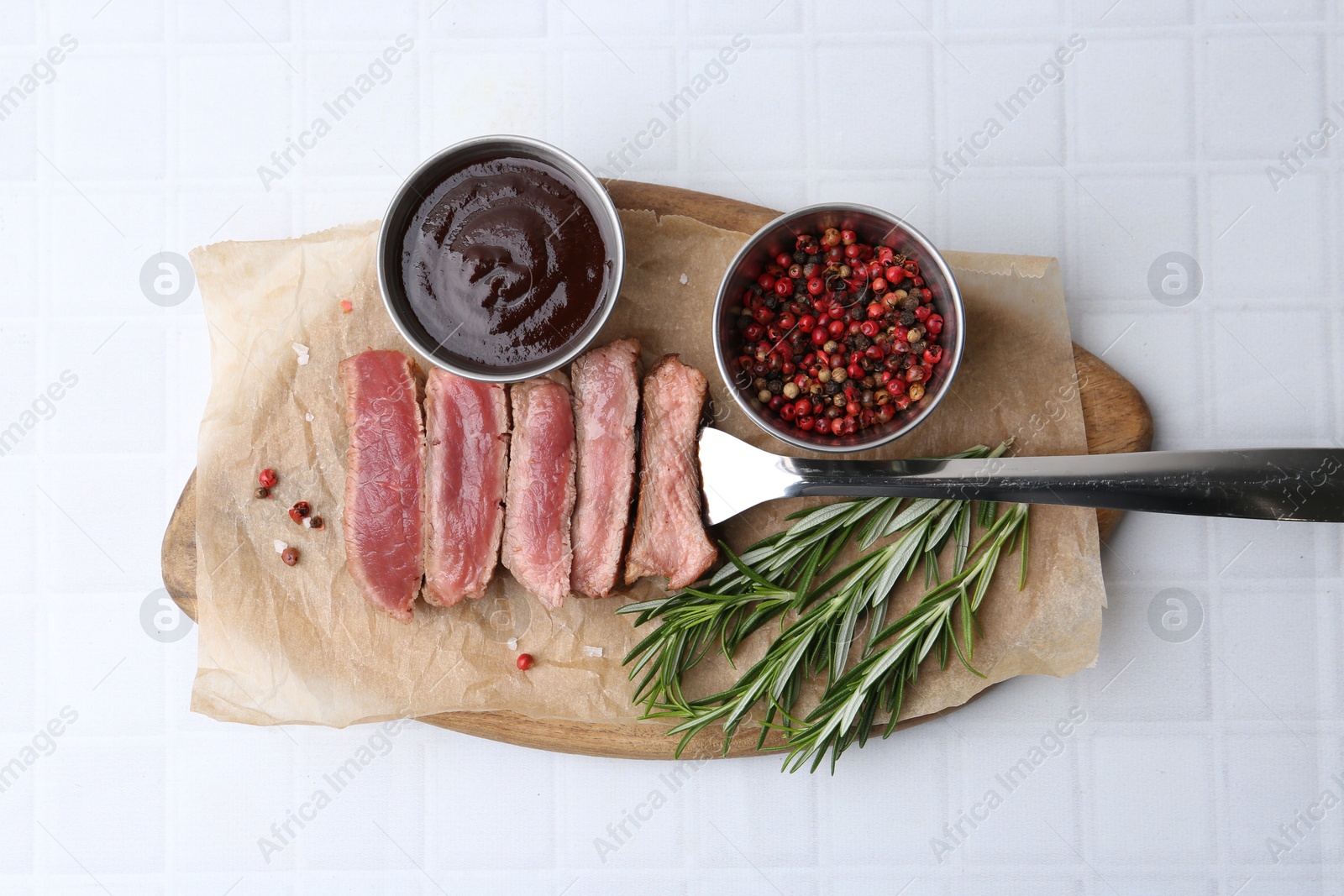 Photo of Delicious sliced beef tenderloin with different degrees of doneness, sauce and spices on light tiled table, top view