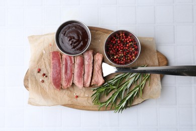 Photo of Delicious sliced beef tenderloin with different degrees of doneness, sauce and spices on light tiled table, top view