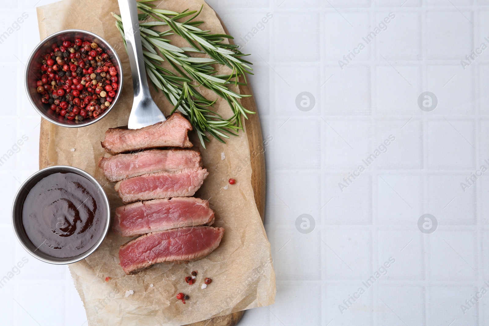 Photo of Delicious sliced beef tenderloin with different degrees of doneness, sauce and spices on light tiled table, top view. Space for text