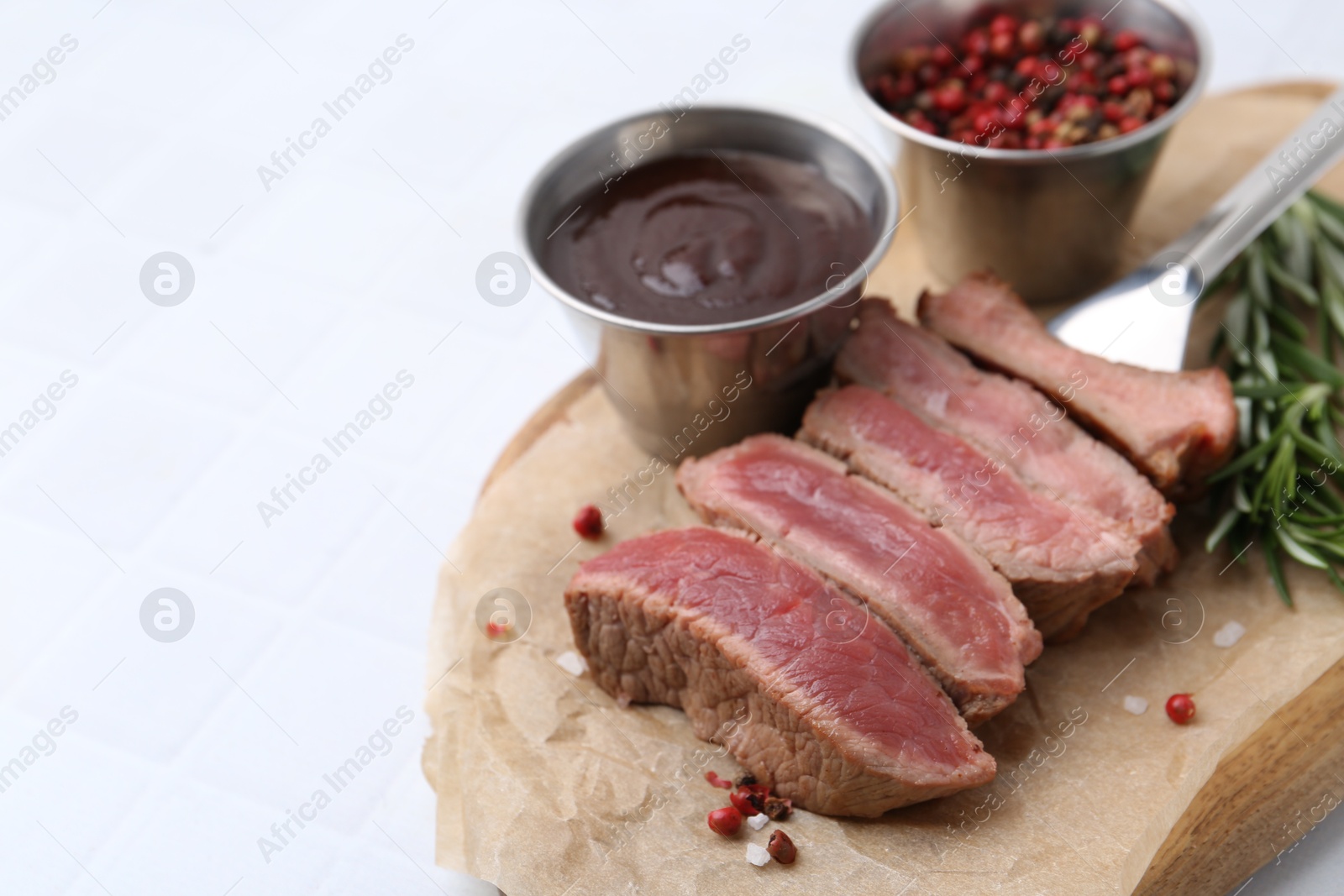 Photo of Delicious sliced beef tenderloin with different degrees of doneness, sauce and spices on light table, closeup. Space for text