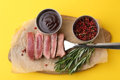 Photo of Delicious sliced beef tenderloin with different degrees of doneness, sauce and spices on yellow table, top view