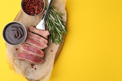 Photo of Delicious sliced beef tenderloin with different degrees of doneness, sauce and spices on yellow table, top view. Space for text