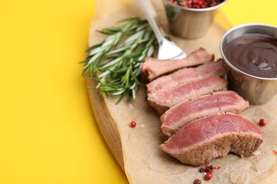 Photo of Delicious sliced beef tenderloin with different degrees of doneness, sauce and spices on yellow table, closeup. Space for text