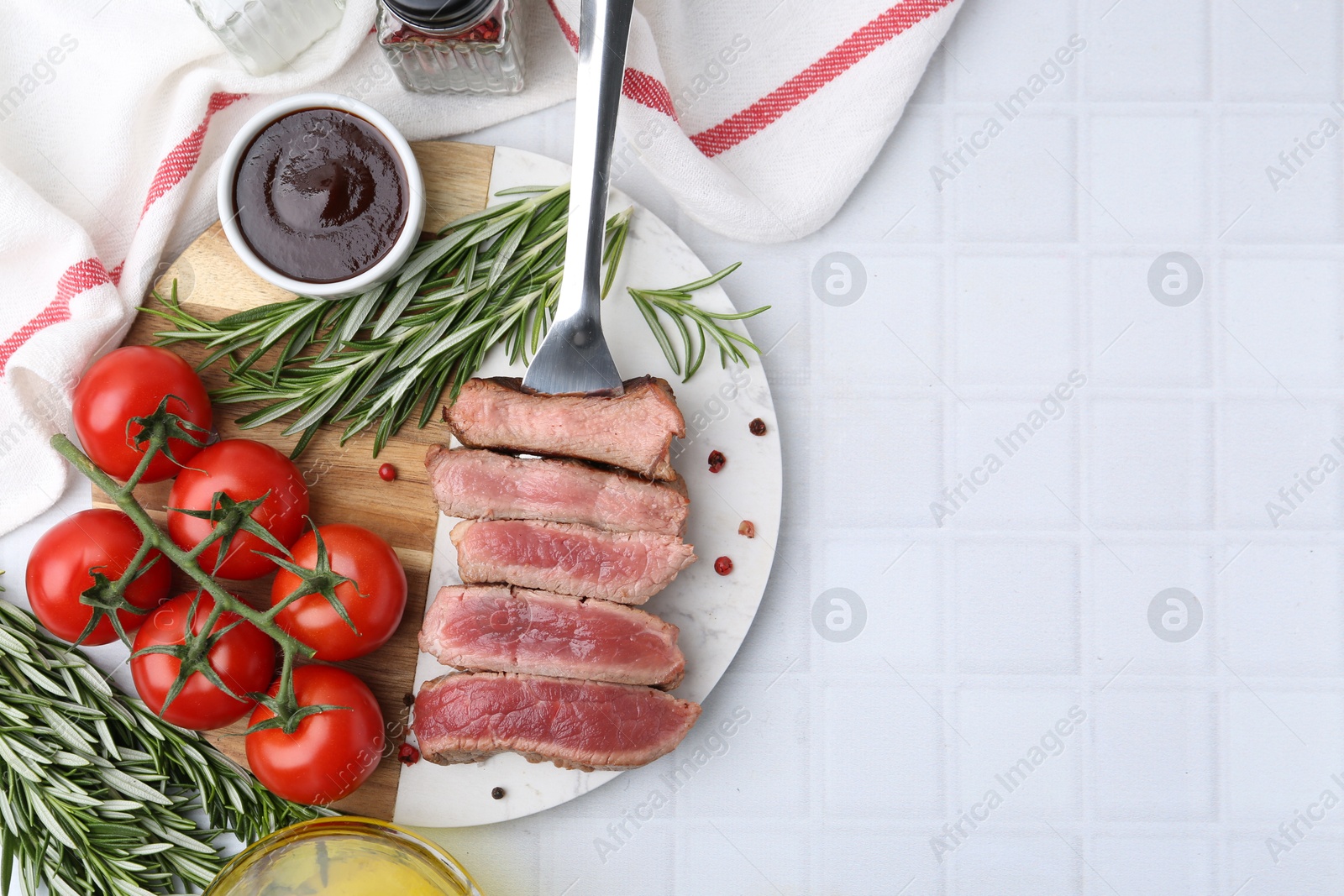 Photo of Delicious sliced beef tenderloin with different degrees of doneness, tomatoes, sauce and spices on light tiled table, top view. Space for text