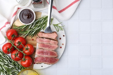 Photo of Delicious sliced beef tenderloin with different degrees of doneness, tomatoes, sauce and spices on light tiled table, top view. Space for text