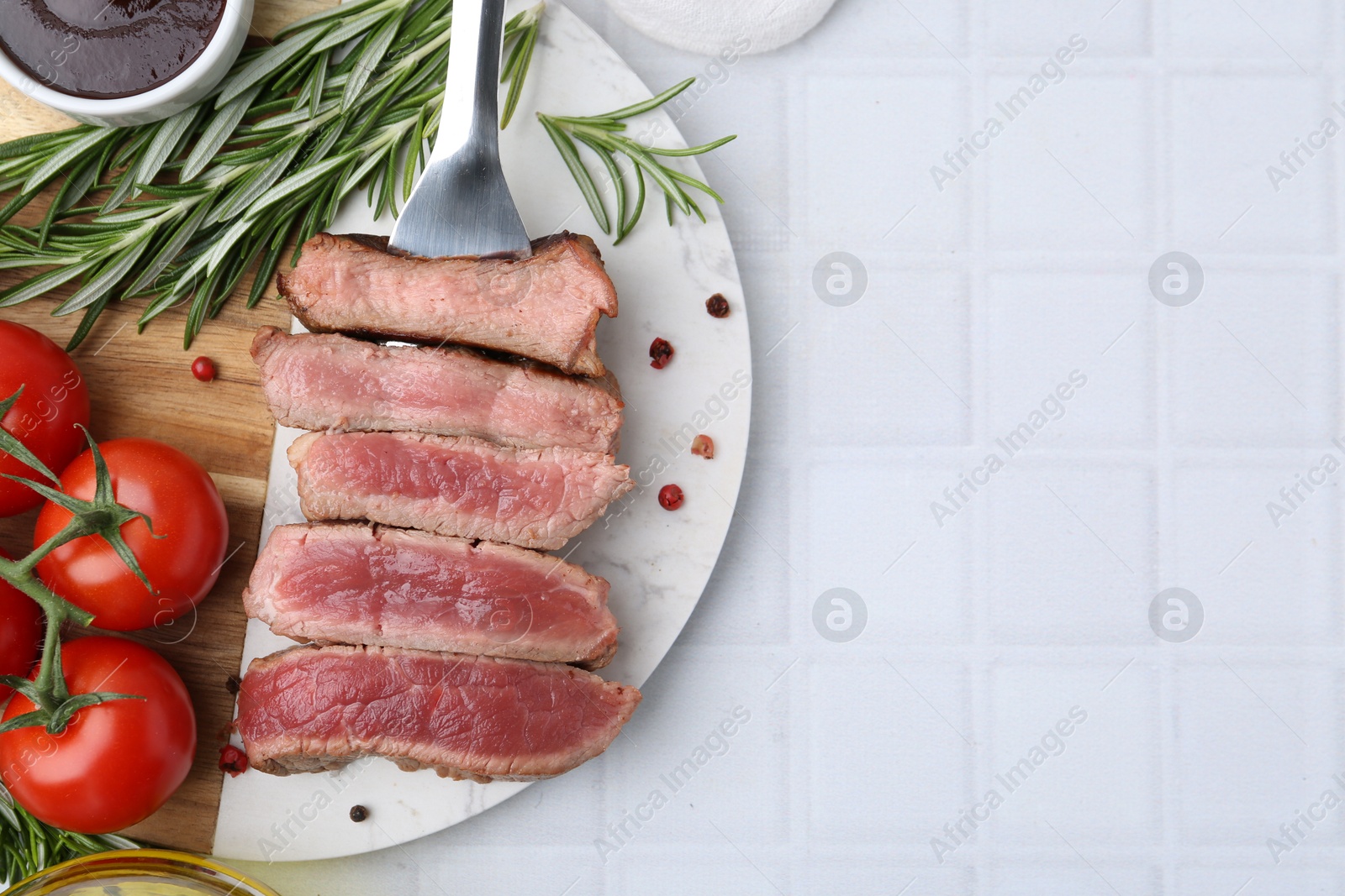 Photo of Delicious sliced beef tenderloin with different degrees of doneness, tomatoes, sauce and spices on light tiled table, top view. Space for text