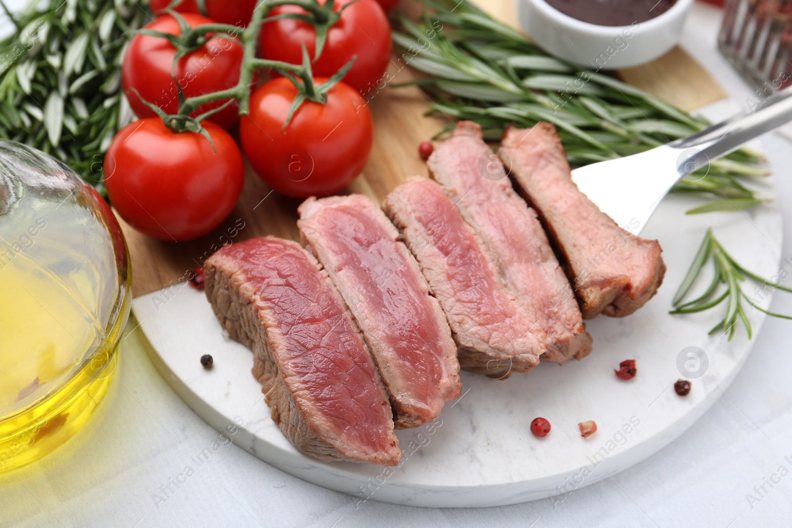 Photo of Delicious sliced beef tenderloin with different degrees of doneness, tomatoes, spices and oil on light table, closeup