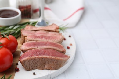 Photo of Delicious sliced beef tenderloin with different degrees of doneness, tomatoes and spices on light tiled table, closeup. Space for text