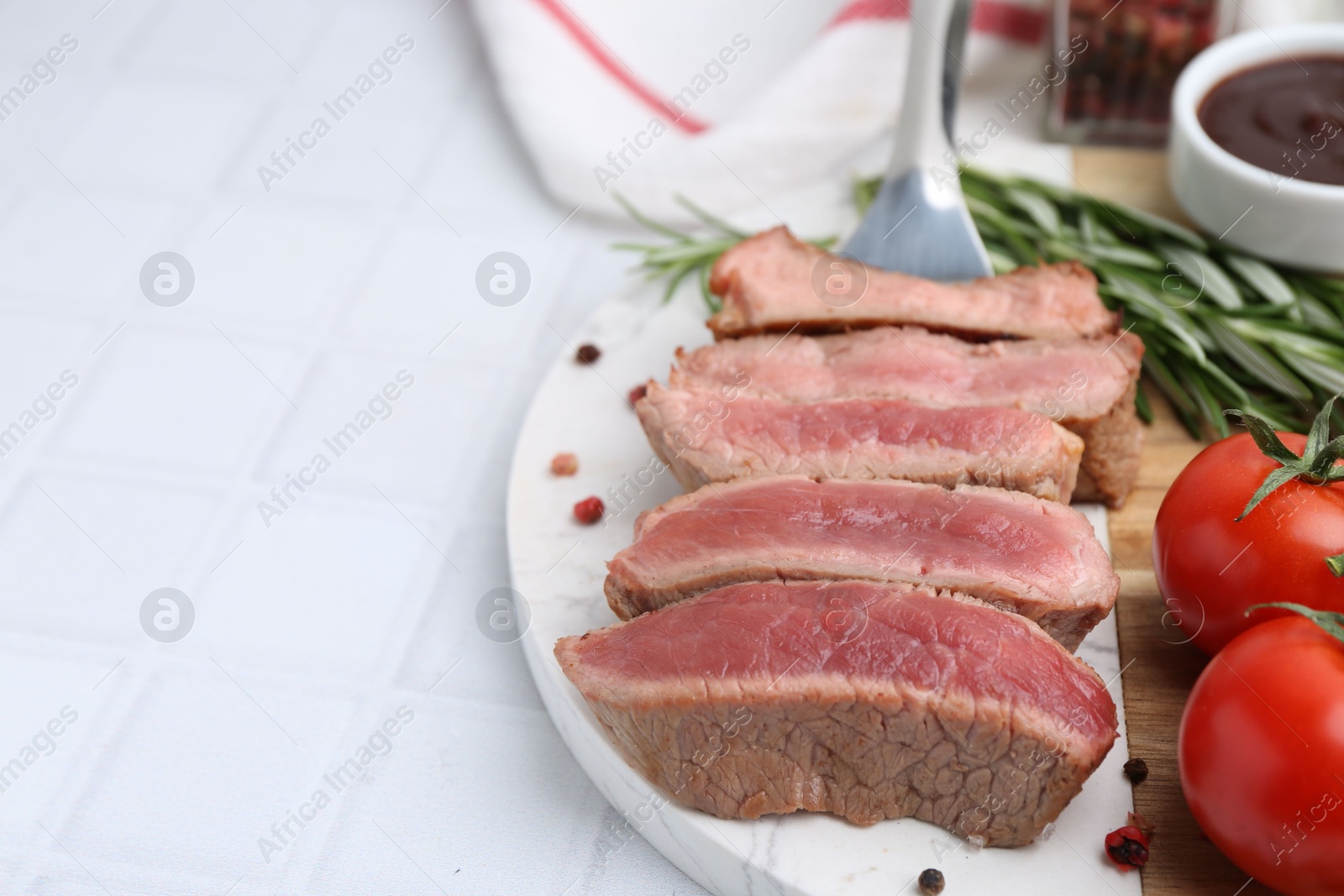 Photo of Delicious sliced beef tenderloin with different degrees of doneness, tomatoes and spices on light tiled table, closeup. Space for text