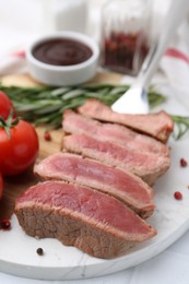 Photo of Delicious sliced beef tenderloin with different degrees of doneness, tomatoes and spices on table, closeup