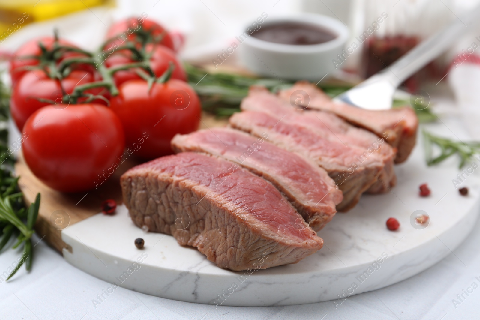 Photo of Delicious sliced beef tenderloin with different degrees of doneness, tomatoes and spices on table, closeup