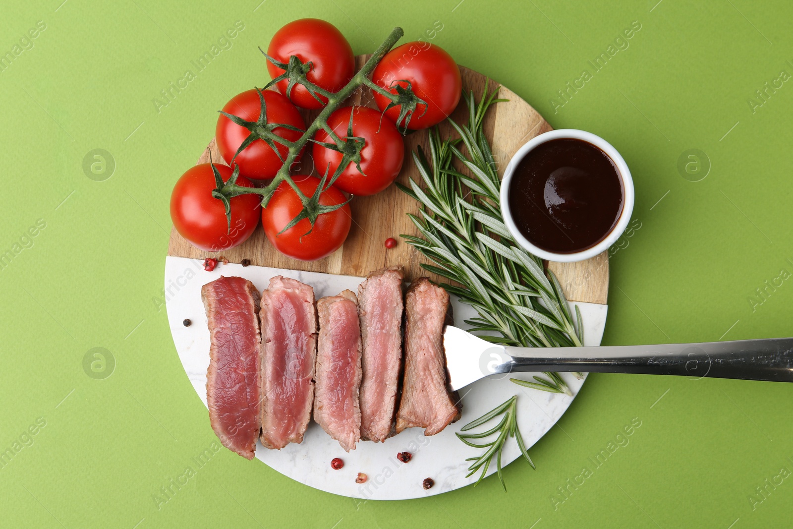 Photo of Delicious sliced beef tenderloin with different degrees of doneness, tomatoes, sauce and spices on green table, top view