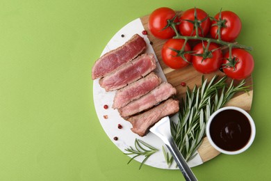 Photo of Delicious sliced beef tenderloin with different degrees of doneness, tomatoes, sauce and spices on green table, top view. Space for text