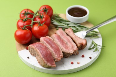 Photo of Delicious sliced beef tenderloin with different degrees of doneness, tomatoes, sauce and spices on green table, closeup