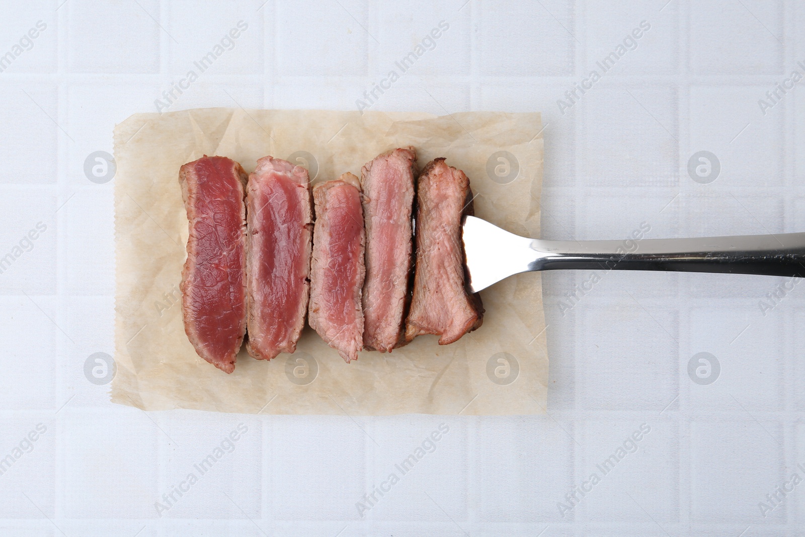 Photo of Delicious sliced beef tenderloin with different degrees of doneness on light tiled table, top view