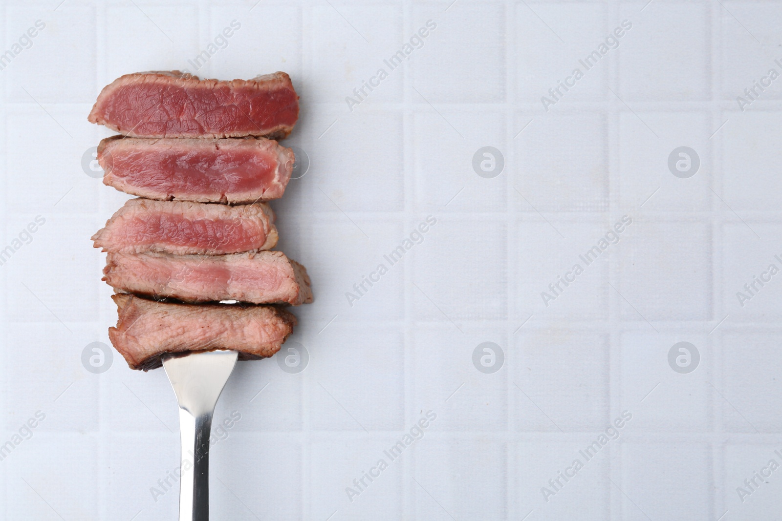 Photo of Delicious sliced beef tenderloin with different degrees of doneness on light tiled table, top view. Space for text